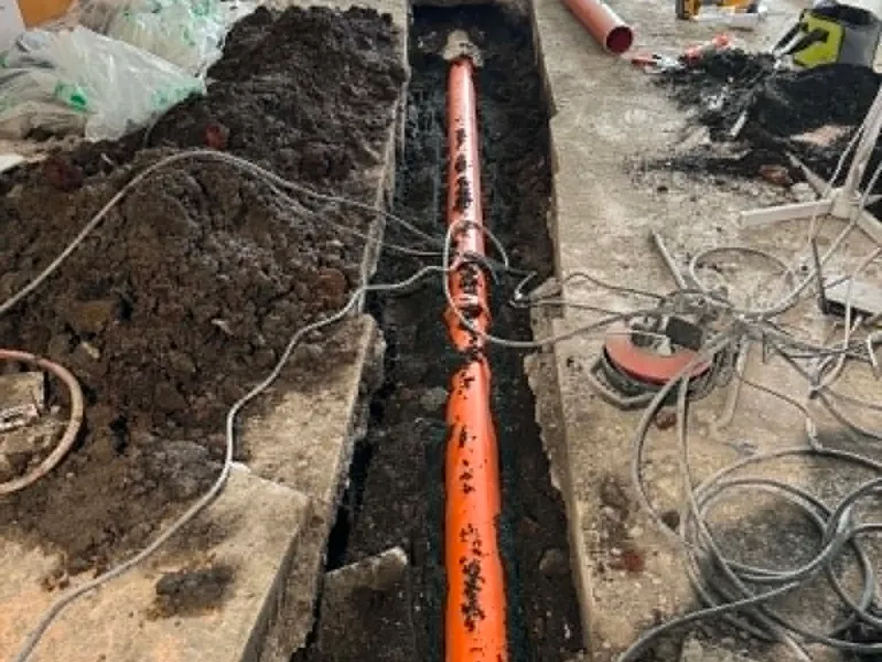 Ný appelsínugul PVC frárennslislögn lögð í mjóa rennu sem söguð hefur verið í steypt gólf í rifnu rými.